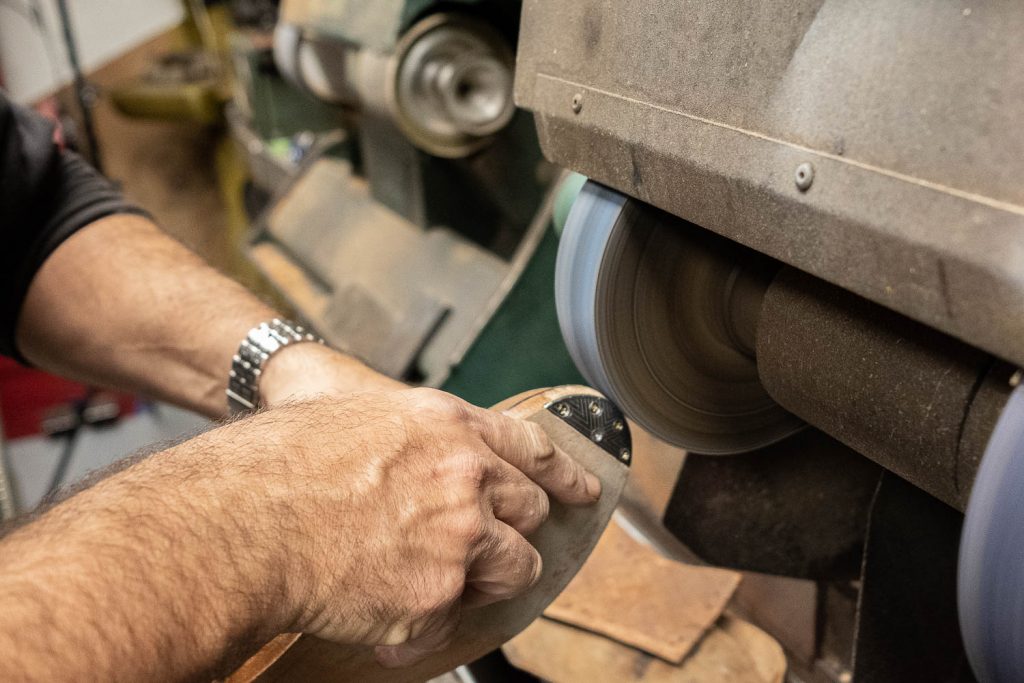 using a machine to sand down the edges of the welt, midsole, and metal toe tap so they are flush