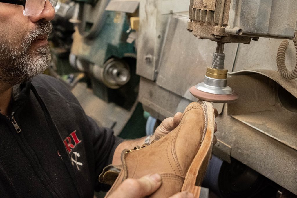 steve doudaklian using a machine to sand down the edges of the welt, midsole, and metal toe tap so they are flush resulting in a fresh new layer of the midsole and outsole edge